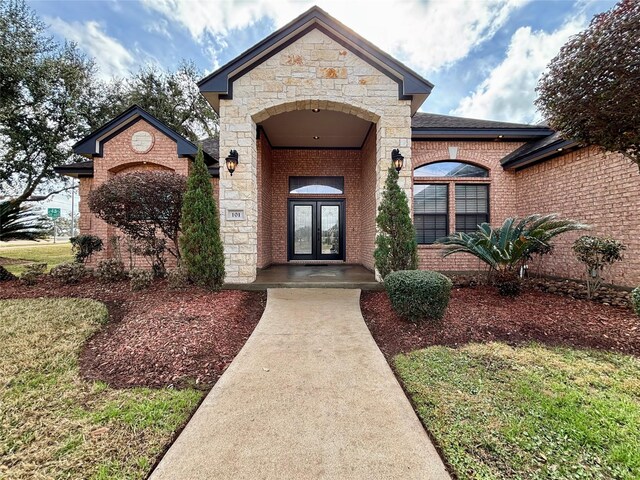 doorway to property featuring stone siding, french doors, and brick siding