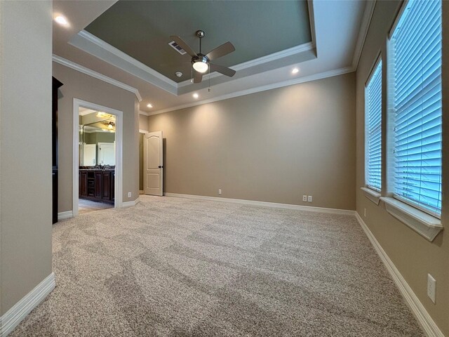 carpeted empty room with a raised ceiling, visible vents, ornamental molding, ceiling fan, and baseboards