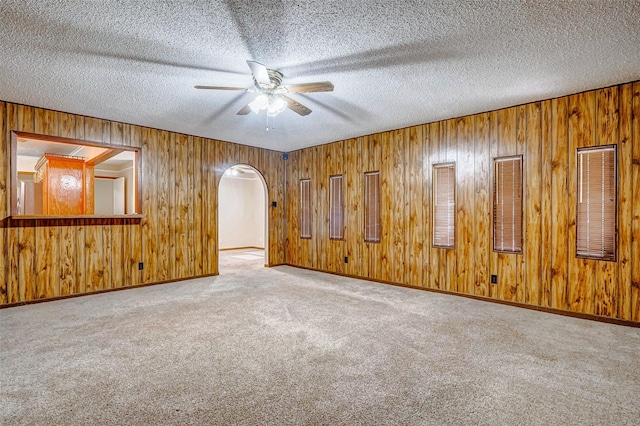 carpeted spare room with ceiling fan, wooden walls, and a textured ceiling