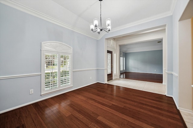 spare room featuring wood-type flooring, crown molding, baseboards, and an inviting chandelier