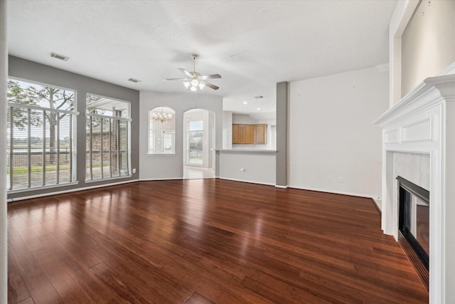 unfurnished living room featuring baseboards, visible vents, a glass covered fireplace, wood finished floors, and ceiling fan with notable chandelier