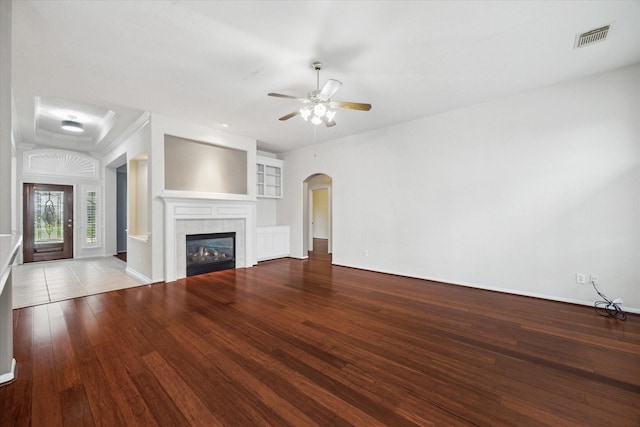 unfurnished living room featuring a tiled fireplace, visible vents, arched walkways, and wood finished floors