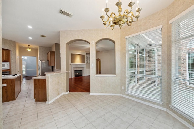 kitchen featuring brown cabinets, light countertops, white microwave, freestanding refrigerator, and light tile patterned flooring