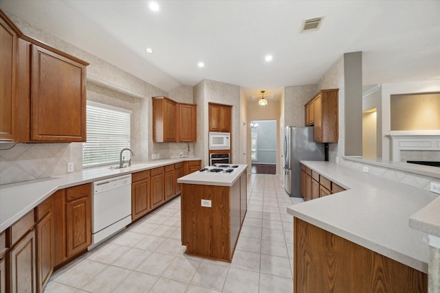 kitchen with white appliances, tasteful backsplash, brown cabinetry, a kitchen island, and a sink