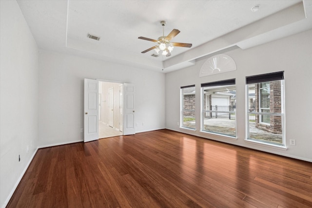 empty room featuring a tray ceiling, visible vents, baseboards, and wood finished floors