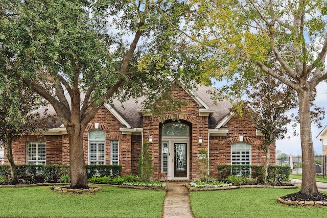 traditional home with a shingled roof, a front yard, and brick siding