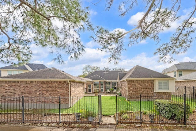 back of house featuring a fenced front yard, a shingled roof, a lawn, and brick siding