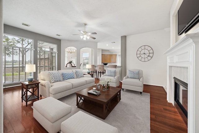 living room with visible vents, baseboards, dark wood finished floors, a glass covered fireplace, and ceiling fan with notable chandelier