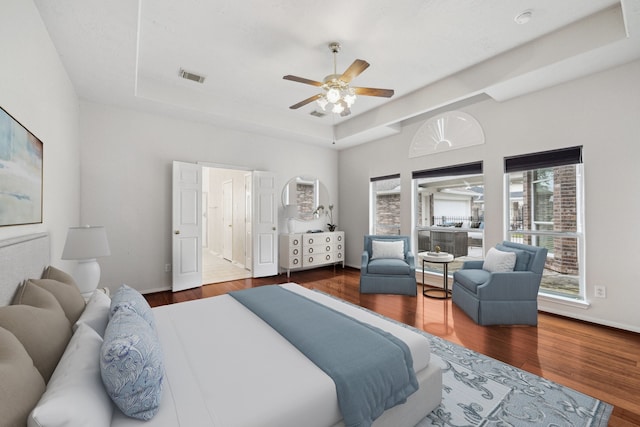 bedroom with baseboards, visible vents, ceiling fan, wood finished floors, and a tray ceiling