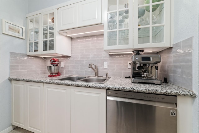 kitchen with tasteful backsplash, white cabinetry, sink, stainless steel dishwasher, and light stone countertops