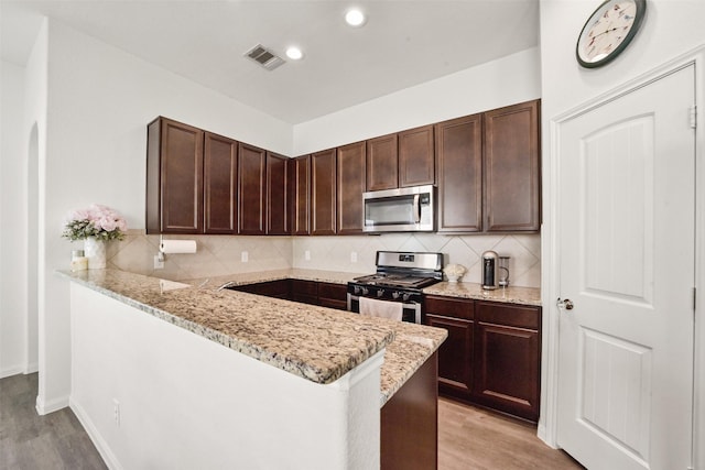 kitchen with decorative backsplash, light stone counters, kitchen peninsula, stainless steel appliances, and light hardwood / wood-style flooring