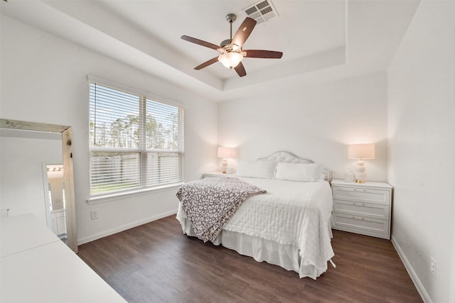 bedroom with dark wood-type flooring, ceiling fan, and a tray ceiling