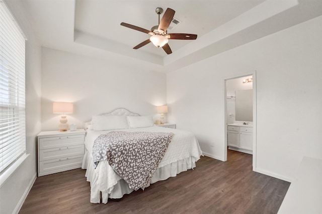 bedroom with dark hardwood / wood-style flooring, connected bathroom, a raised ceiling, and ceiling fan