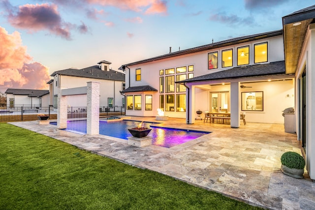 back of property at dusk featuring a patio, fence, a yard, a fenced in pool, and stucco siding