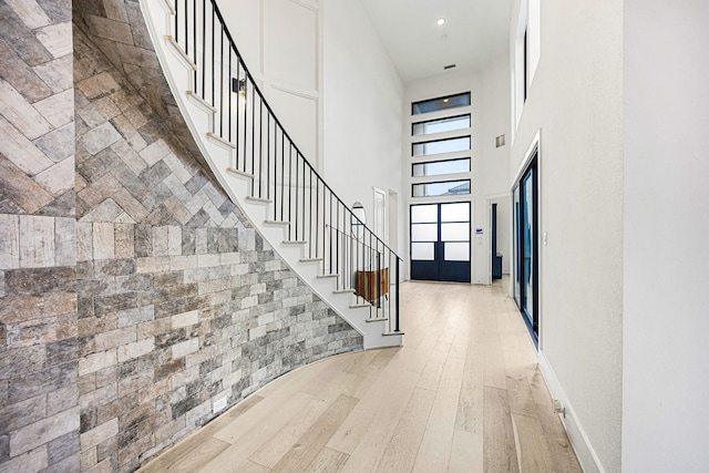 entrance foyer featuring stairs, a high ceiling, light wood-type flooring, and baseboards