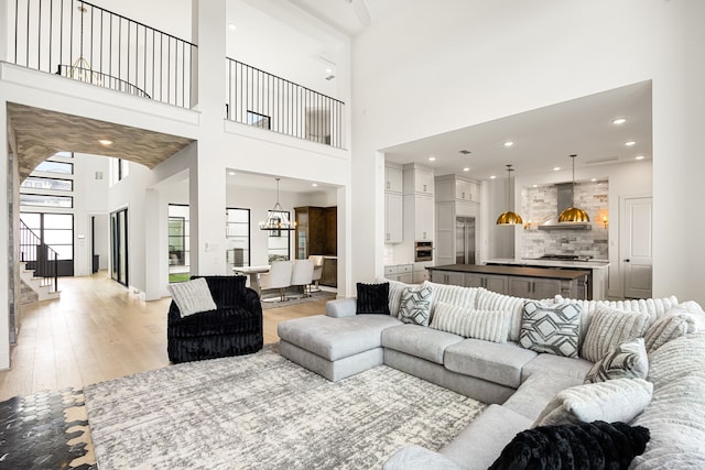 living area featuring stairway, recessed lighting, light wood-style flooring, and a towering ceiling