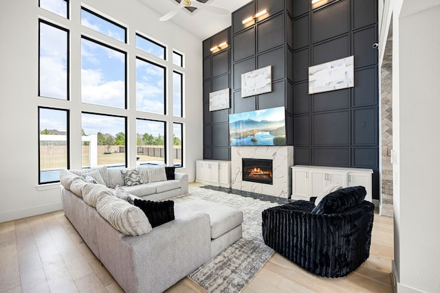 living room with a decorative wall, a high ceiling, a fireplace, baseboards, and light wood-type flooring