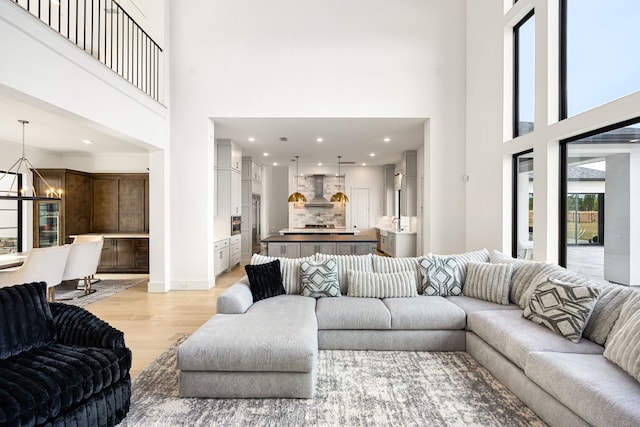 living area with a notable chandelier, recessed lighting, a towering ceiling, light wood-type flooring, and baseboards