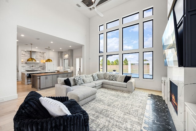 living room with light wood finished floors, baseboards, ceiling fan, a premium fireplace, and a high ceiling