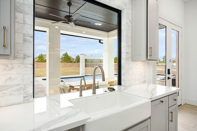 kitchen featuring ceiling fan, gray cabinetry, a sink, light wood-style floors, and light stone countertops