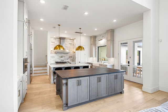 kitchen featuring tasteful backsplash, visible vents, wall chimney range hood, and gray cabinetry