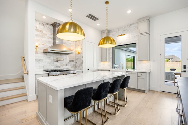 kitchen with tasteful backsplash, visible vents, a kitchen island, light wood-type flooring, and wall chimney range hood