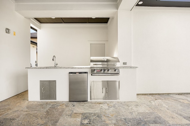 kitchen with stone finish flooring, a sink, and freestanding refrigerator