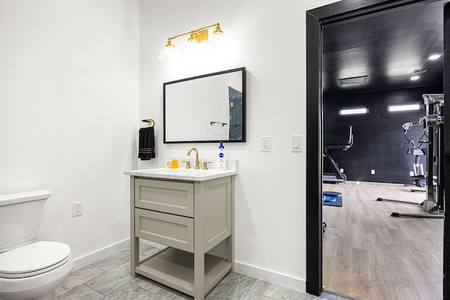 bathroom with toilet, baseboards, wood finished floors, and vanity