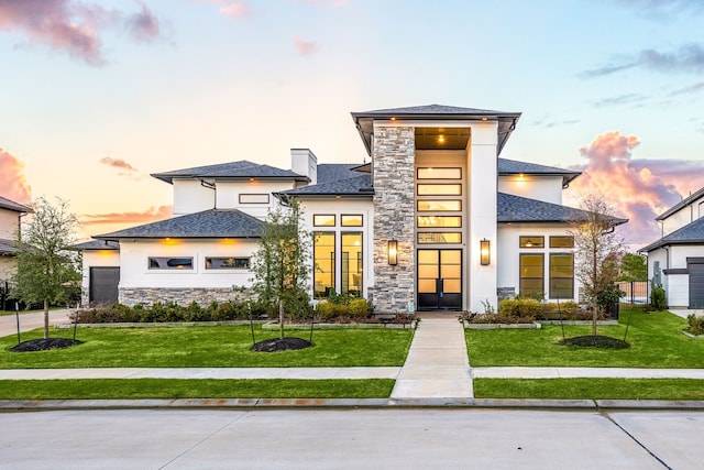 prairie-style home featuring a garage, stone siding, a lawn, and stucco siding