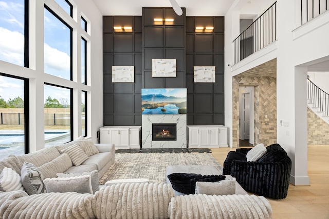 living area with a decorative wall, a towering ceiling, a high end fireplace, stairway, and light wood-type flooring