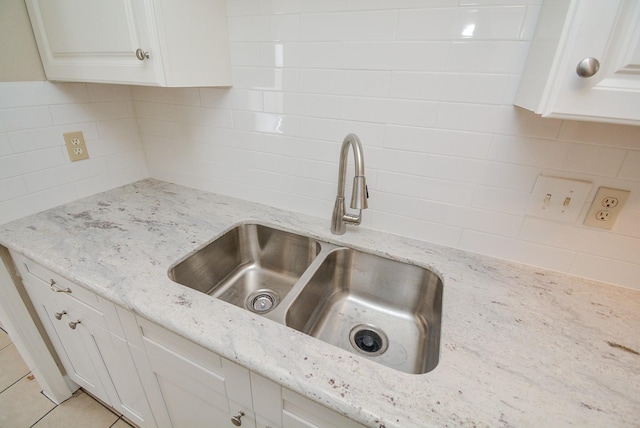 details featuring light stone countertops, sink, white cabinets, and backsplash