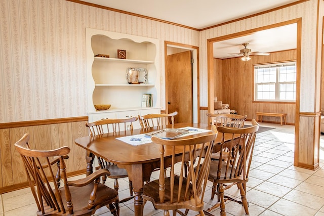 dining room with wood walls, ornamental molding, light tile patterned floors, ceiling fan, and built in shelves