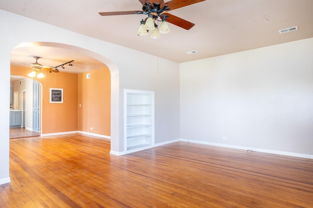 empty room featuring ceiling fan, wood-type flooring, track lighting, and built in features