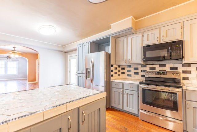 kitchen with tasteful backsplash, gray cabinets, light hardwood / wood-style flooring, and appliances with stainless steel finishes