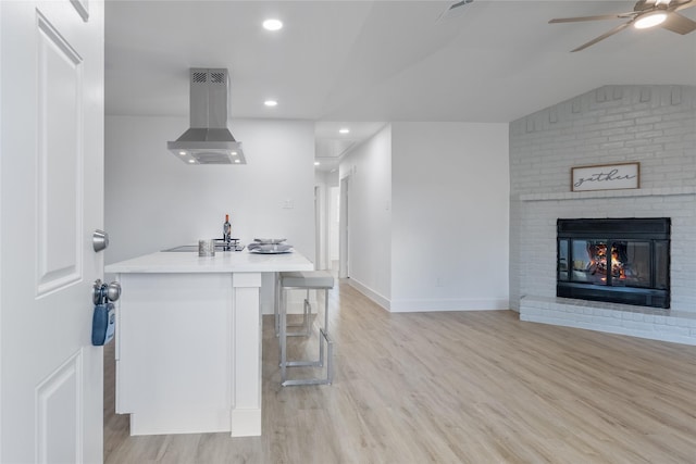 kitchen featuring a brick fireplace, island range hood, light hardwood / wood-style floors, and a breakfast bar