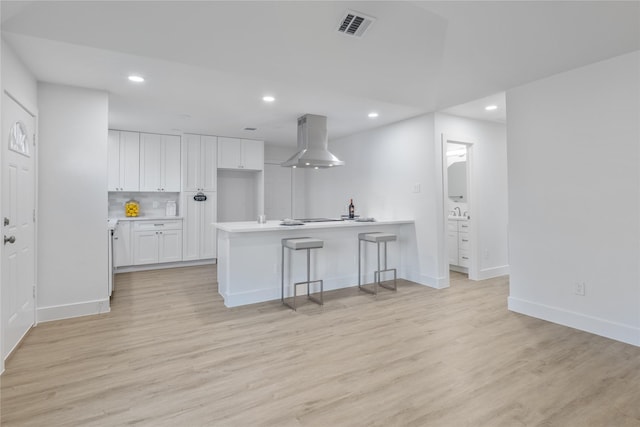 kitchen with white cabinetry, island exhaust hood, a breakfast bar area, and light wood-type flooring