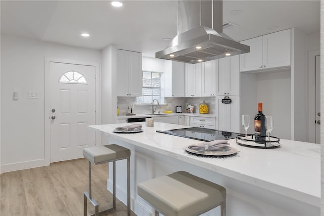 kitchen featuring island range hood, white cabinetry, sink, a kitchen breakfast bar, and light stone counters