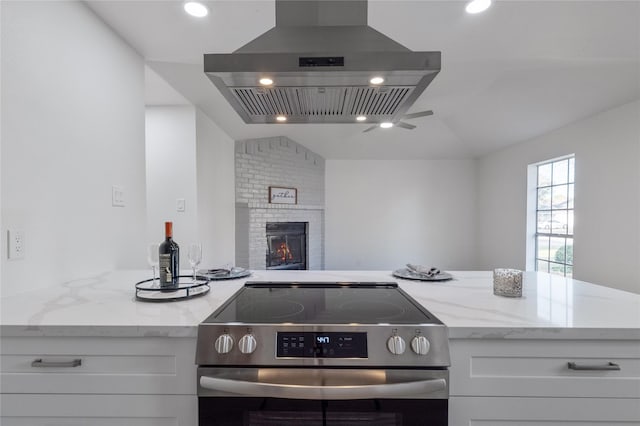 kitchen featuring white cabinets, island range hood, light stone countertops, and electric range