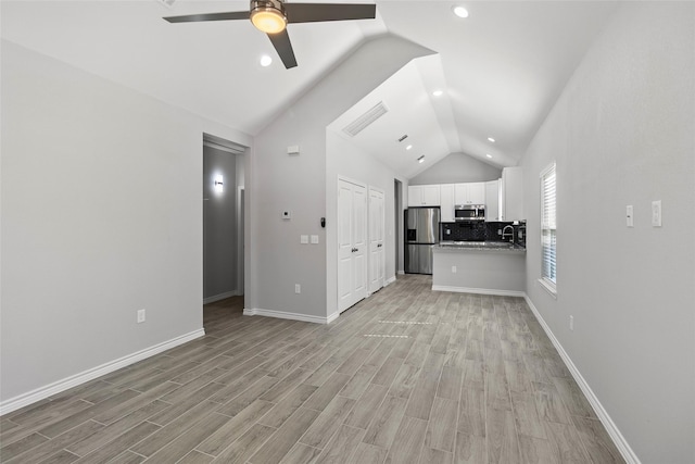 unfurnished living room with ceiling fan, lofted ceiling, sink, and light hardwood / wood-style floors