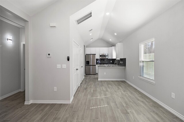 kitchen featuring lofted ceiling, white cabinetry, stainless steel appliances, light stone countertops, and decorative backsplash