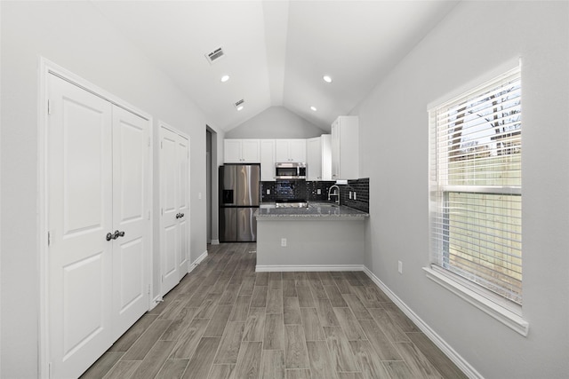 kitchen featuring appliances with stainless steel finishes, lofted ceiling, white cabinets, backsplash, and light stone countertops