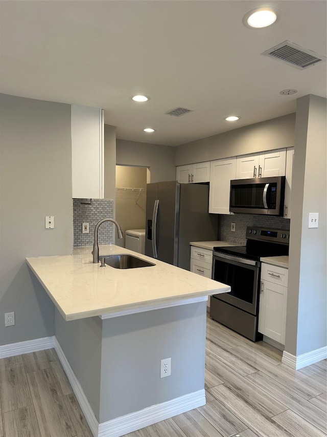 kitchen with sink, white cabinetry, stainless steel appliances, decorative backsplash, and kitchen peninsula