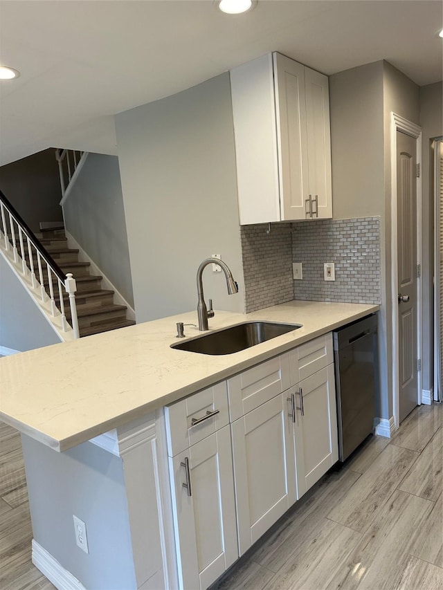 kitchen featuring dishwasher, sink, white cabinets, decorative backsplash, and light wood-type flooring