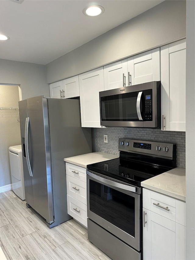 kitchen featuring white cabinetry, tasteful backsplash, light wood-type flooring, appliances with stainless steel finishes, and washer and clothes dryer