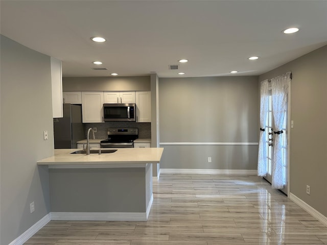 kitchen featuring sink, appliances with stainless steel finishes, kitchen peninsula, decorative backsplash, and white cabinets