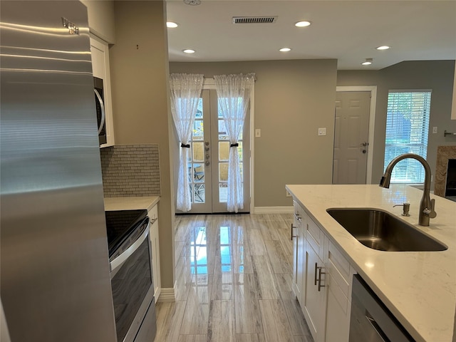 kitchen featuring sink, white cabinetry, stainless steel appliances, light stone countertops, and french doors