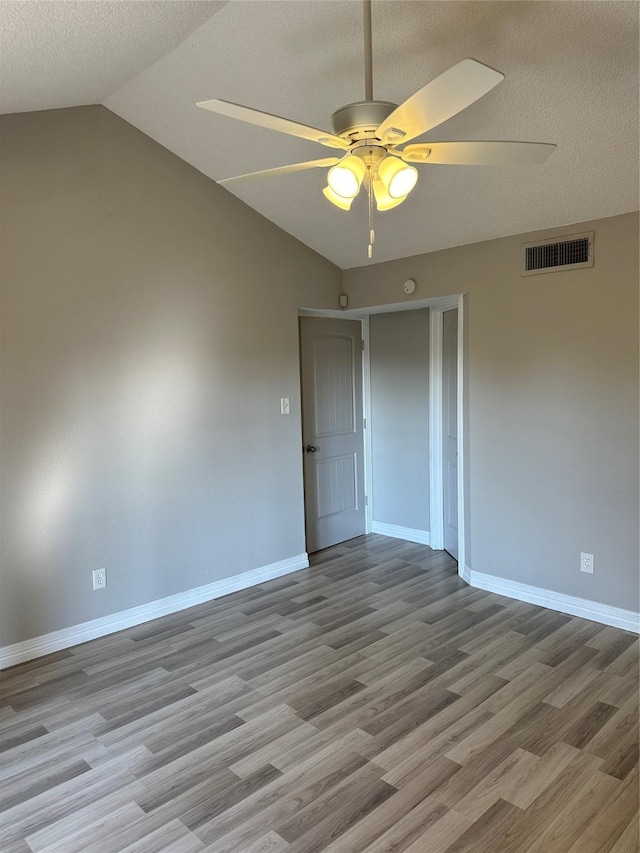 unfurnished room with a textured ceiling, vaulted ceiling, light hardwood / wood-style floors, and ceiling fan