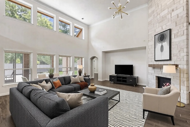 living room with a chandelier, ornamental molding, dark hardwood / wood-style floors, a towering ceiling, and a fireplace