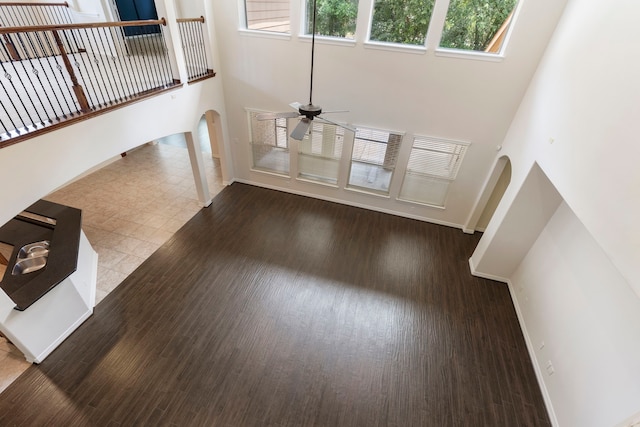 unfurnished living room featuring ceiling fan, a towering ceiling, and light wood-type flooring