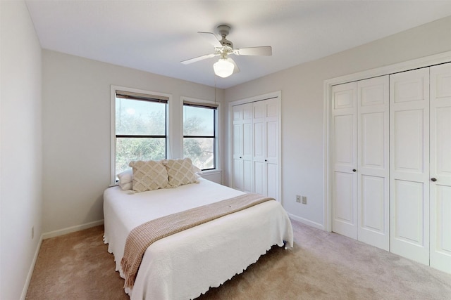 bedroom featuring multiple closets, light colored carpet, and ceiling fan